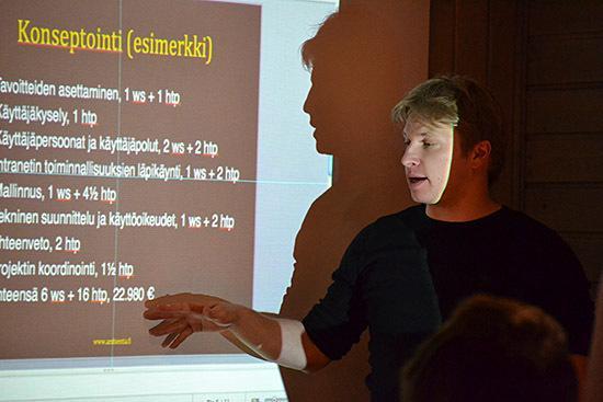 Kari Kinnunen giving a presentation in front of a blue background screen.